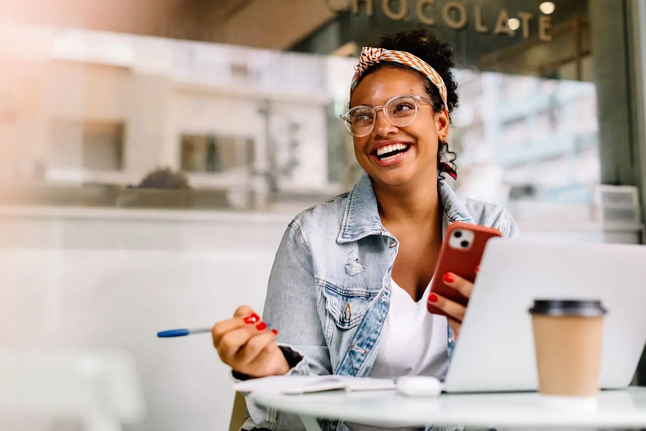 A young woman working on a laptop in a coffee shop, smiling