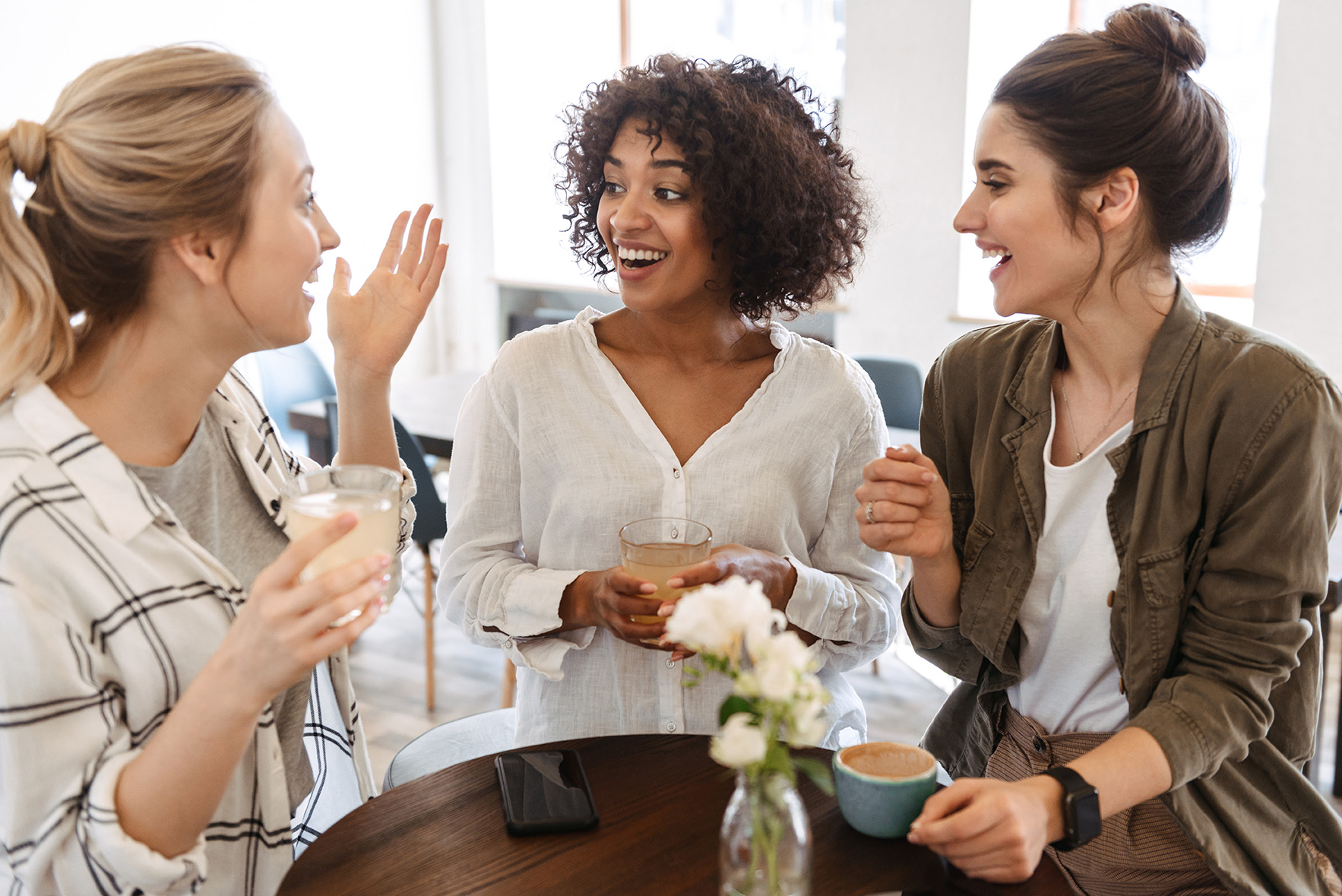 Three women having coffee and chatting, reflecting the good feeling of referring a friend.