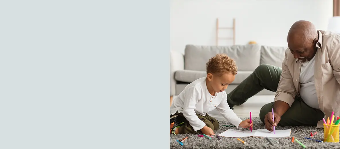 A grandfather and grandson sitting together on the floor drawing, reflecting secure retirement