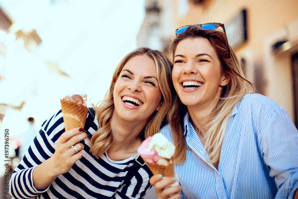 Two friends enjoying ice cream and smiling on a sunny day