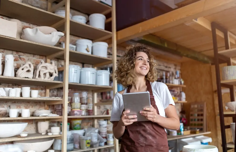 A business owner standing in her shop holding a tablet and smiling