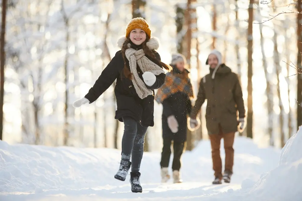 A girl in a winter coat walking ahead of her parents smiling