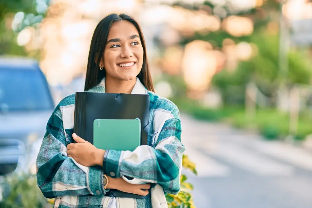 A student holding her notebooks and smiling