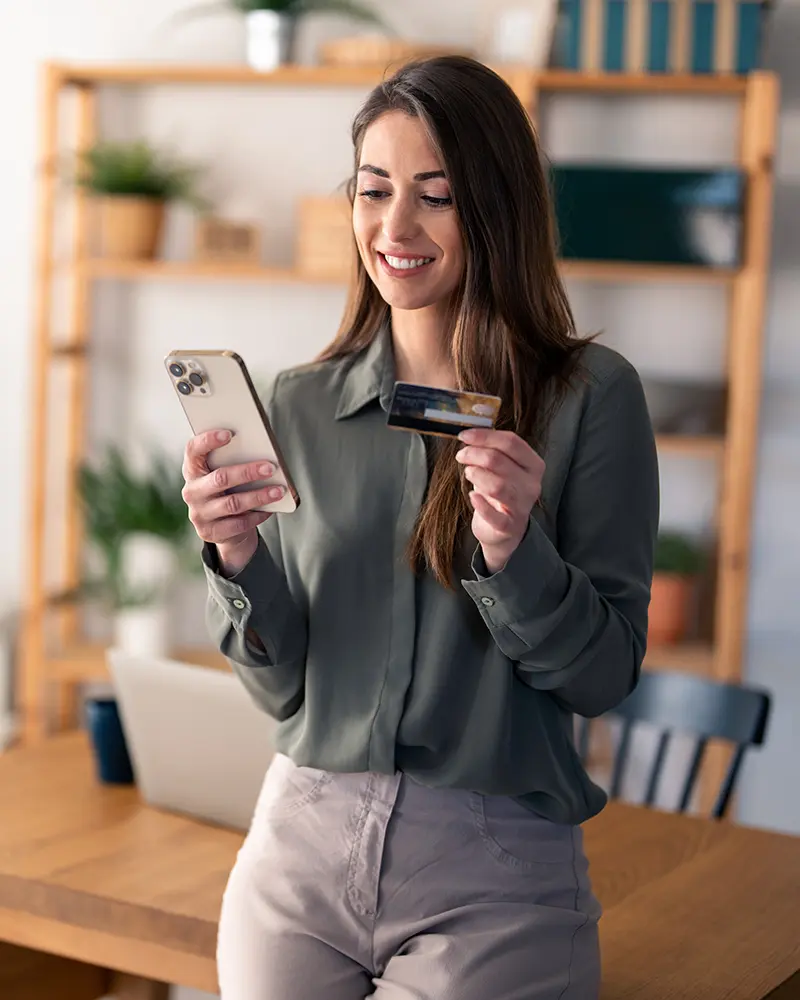 A woman holding her phone and a credit card standing inside a shop