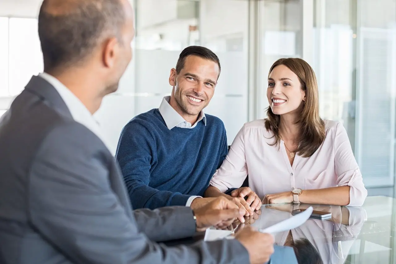 A couple in a meeting smiling, considering security for their investments
