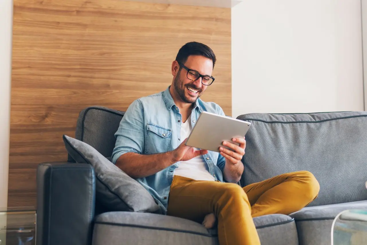 A man smiling look at his tablet, considering investment rates